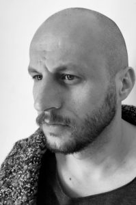 Tomasz Borkowski aktor. Portret mężczyzny z profilu. Ma zarost - brodę i wąsy. Jest łysy.