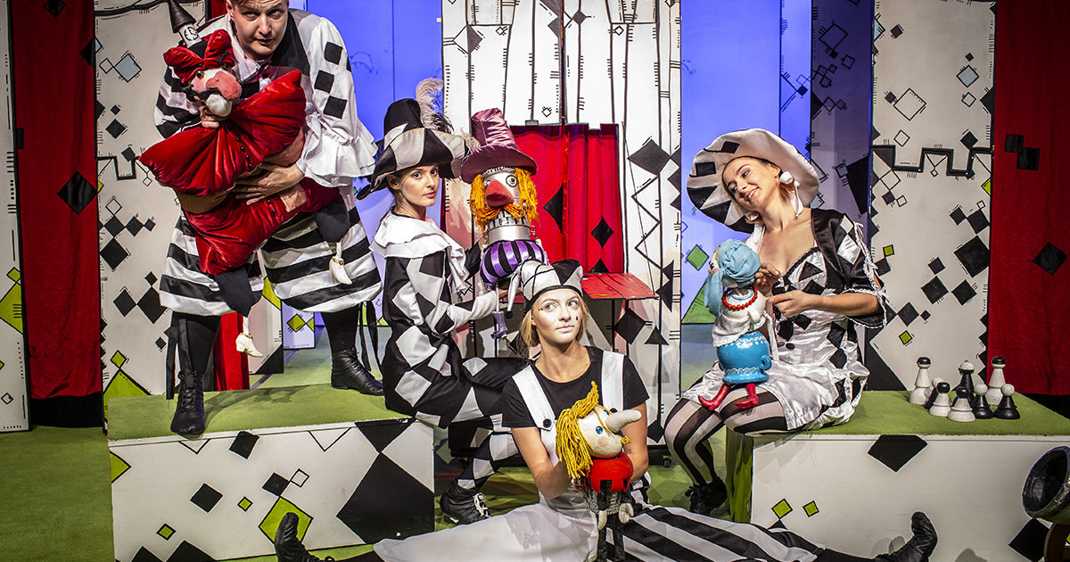 Grupa aktorów w kostiumach z lalkami pozuje na tle dekoracji