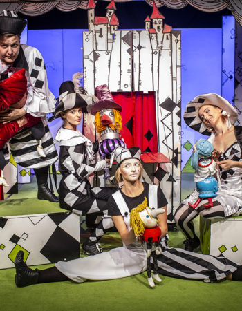 Grupa aktorów w kostiumach z lalkami pozuje na tle dekoracji
