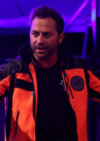 aktor widziany od pasa w górę ubrany w uniform ratowniczy w gumowych rękawiczkach na dłoniach w pozycji jakby odsuwał od siebie innych